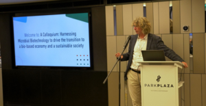Presenter at a podium infront of a screen displaying the title of the meeting
